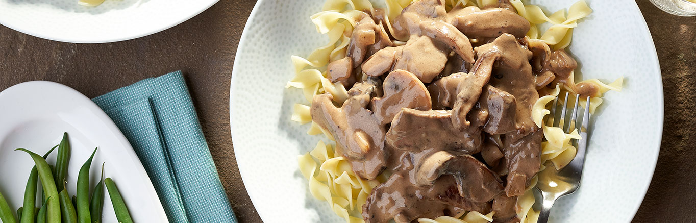 An image of prepared Triple Mushroom Beef Stroganoff made with beef sirloin steak, onion, white mushrooms, shiitake mushrooms, portobello mushrooms, Swanson® Beef Broth, red wine and sour cream.