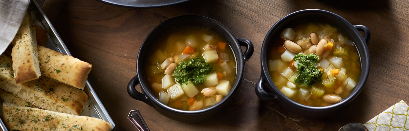 An image of prepared Vegetable Bean Soup with Fresh Pesto made with carrots, potatoes, turnip, leeks, celery, Swanson® Vegetable Broth, cannellini beans, basil, Parmesan and garlic.