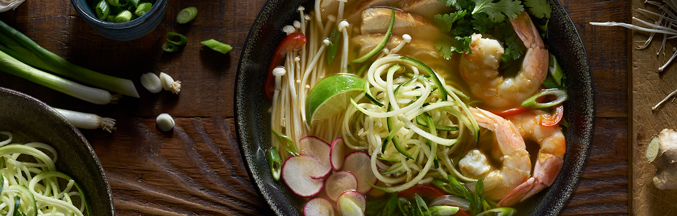 An image of prepared Vietnamese Pho made with onion, red bell pepper, Swanson® Chicken Broth, zucchini, green onion, enoki mushrooms, radish, chicken, shrimp, cilantro and lime.