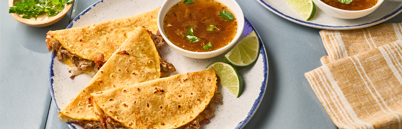 An image of prepared Shortcut Birria Tacos made with steak, Swanson® Spicy Beef Broth, corn tortillas, Oaxaca or mozzarella cheese and cilantro.