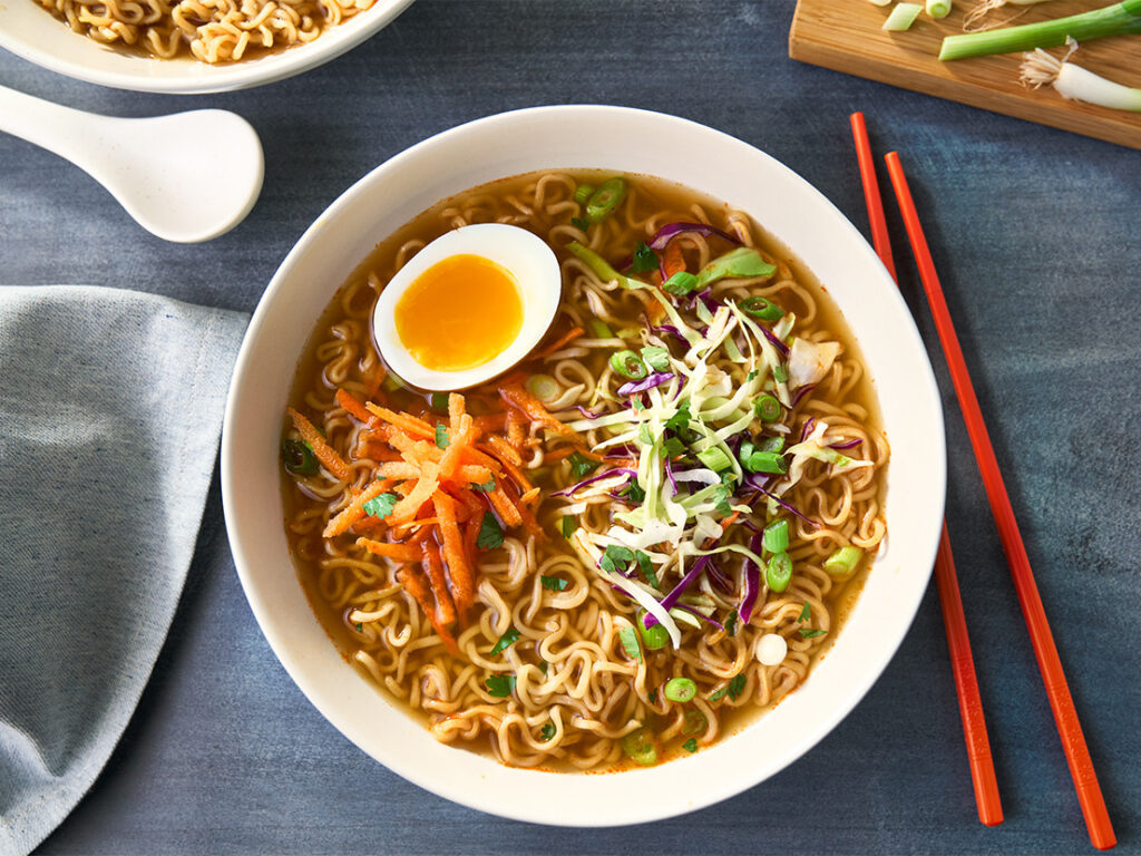 An image of prepared 15-Minute Spicy Chicken Ramen made with garlic, ginger, Swanson® Spicy Chicken Broth, ramen noodles, chicken, Asian slaw mix or broccoli slaw and hard cooked eggs.
