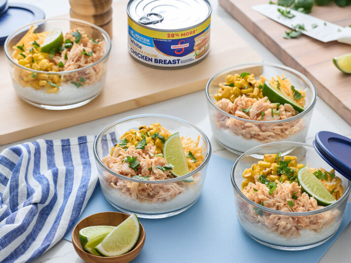 An image of prepared High-Protein Street Corn Chicken Bowls made with Swanson® Premium White Chicken Breast in Water, cottage cheese, corn, Monterey Jack cheese, cilantro and lime wedges.