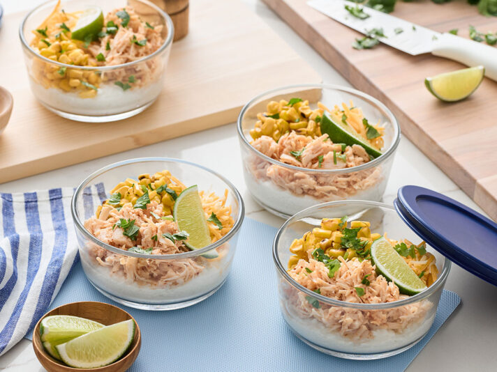 An image of prepared High-Protein Street Corn Chicken Bowls made with Swanson® Premium White Chicken Breast in Water, cottage cheese, corn, Monterey Jack cheese, cilantro and lime wedges.