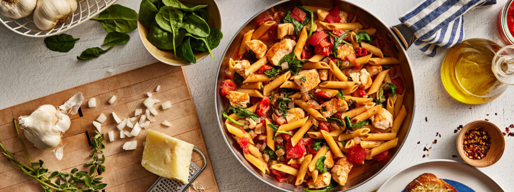 An image of prepared One-Pan Chicken & Pasta Romano made with chicken, canned diced tomatoes, Swanson® Chicken Broth, penne pasta and baby spinach.