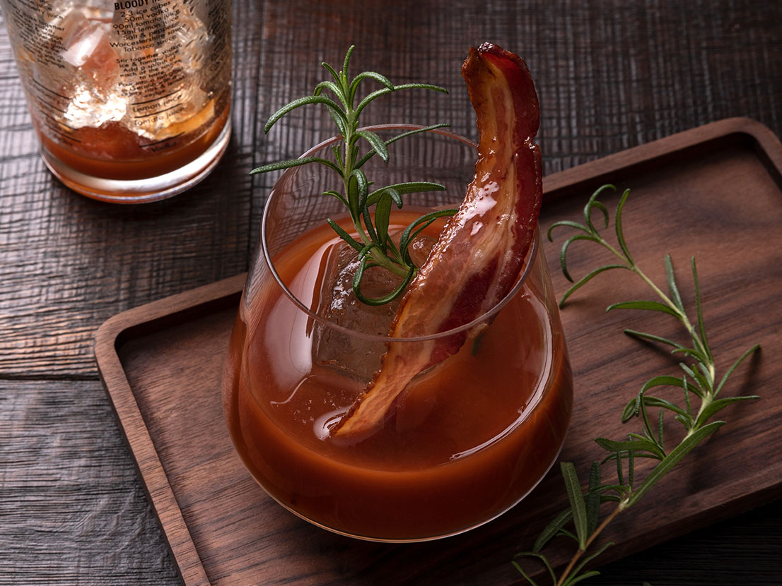 An image of prepared Bourbon and Bacon Bloody Mary made with V8® 100% Vegetable Juice, bourbon, maple syrup, bacon and rosemary.