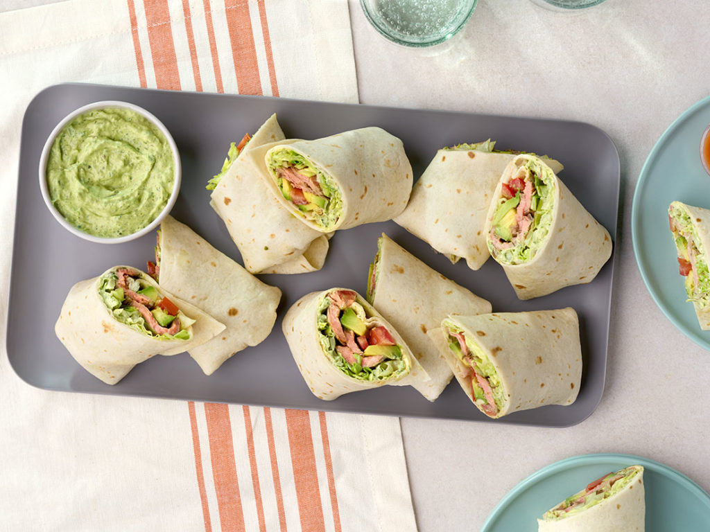 An image of prepared Chimichurri Steak Wraps showing flank steak with creamy chimichurri sauce, avocado, lettuce and tomato wrapped in a flour tortilla.