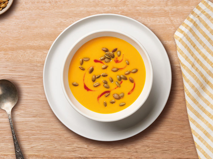 An image of prepared Coconut Carrot Ginger Soup showing a soup made with onion, ginger root, carrots, Swanson® Natural Goodness® Chicken Broth, Campbell's® Condensed Cream of Chicken, coconut milk and sriracha.