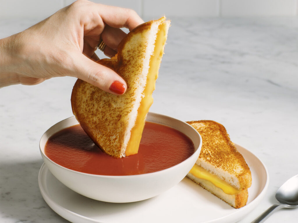 Grilled cheese dunking into a bowl of Campbell's Tomato Soup